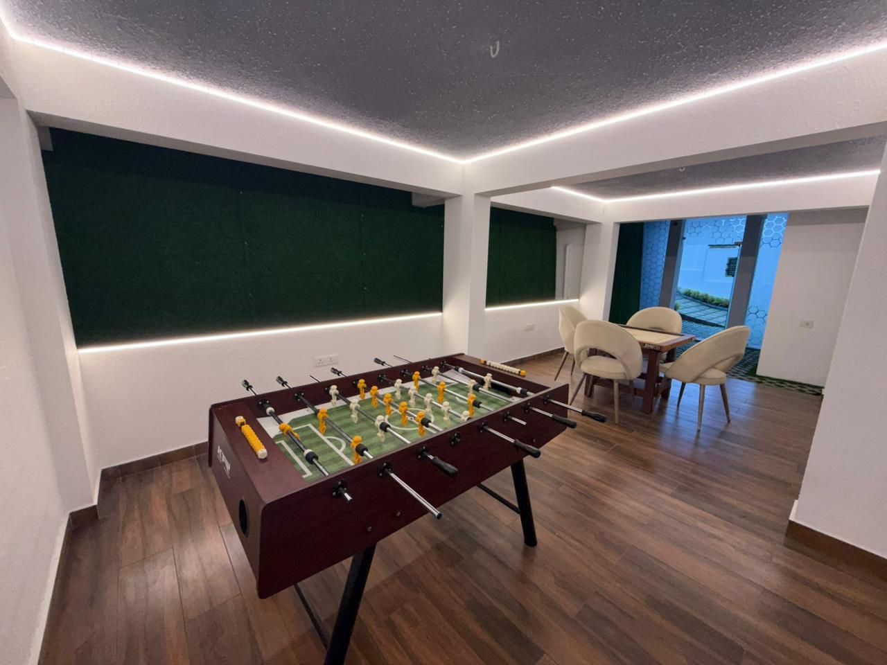 A modern room with a foosball table, a dining area with chairs, and a view through a window.