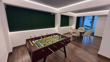 A modern room with a foosball table, a dining area with chairs, and a view through a window.