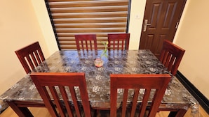 Une table de salle à manger rectangulaire, recouverte d’une nappe à motifs floraux, entourée de six chaises en bois.