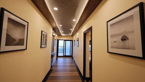 Un couloir aux murs ornés de tableaux encadrés, doté d’un plancher en bois et d’un plafond pourvu d’un éclairage encastré.