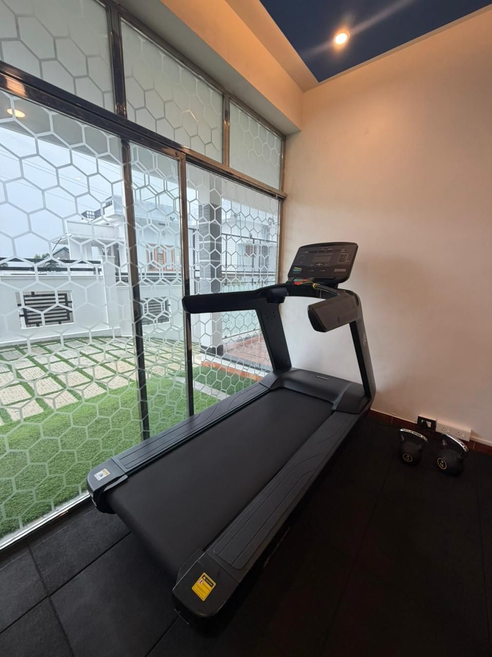 A treadmill in a room with a large window, a ceiling light, and a small exercise ball.