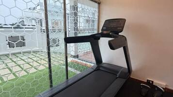 A treadmill in a room with a large window, a ceiling light, and a small exercise ball.
