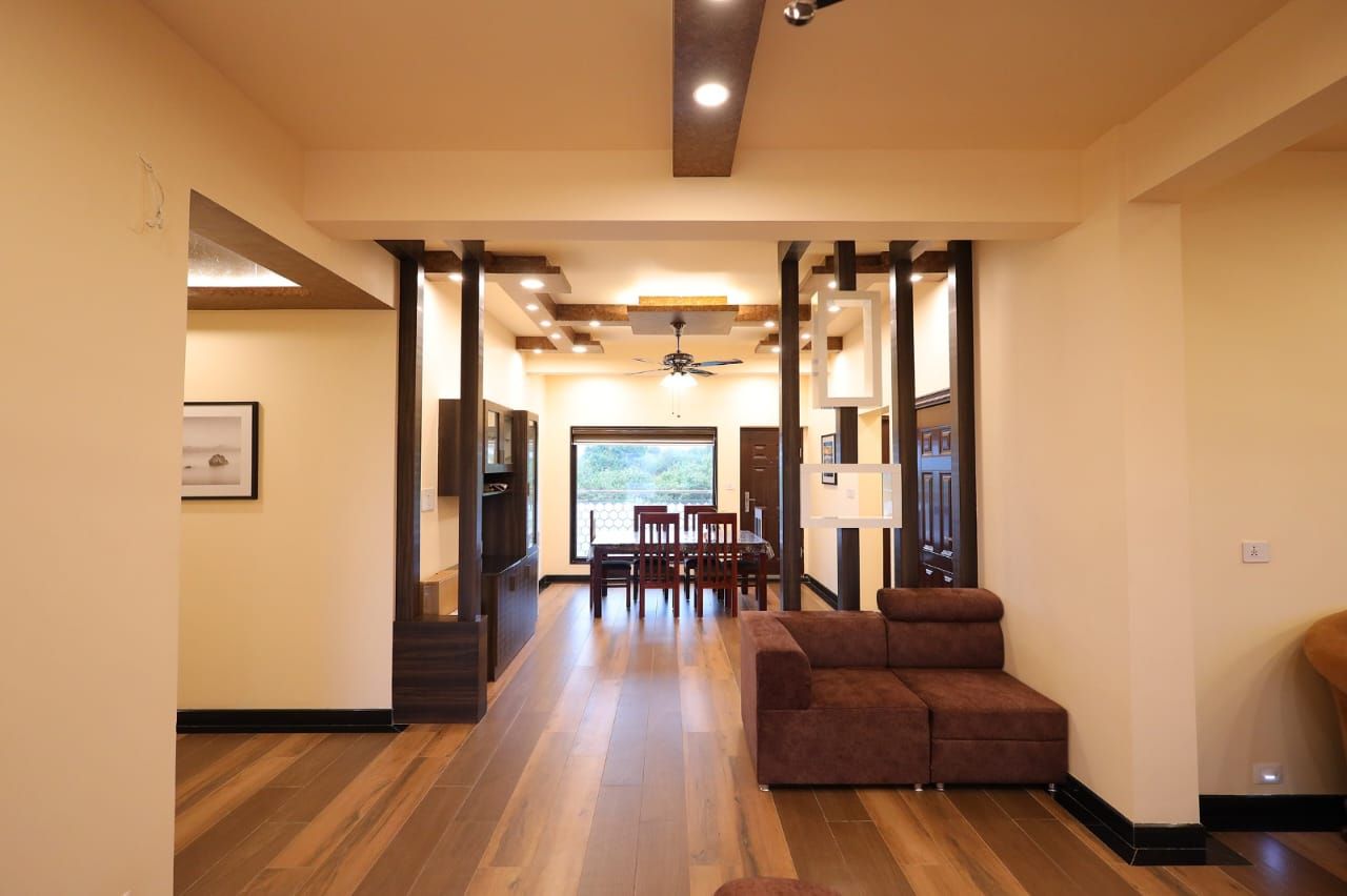 A spacious interior with a wooden floor, a brown sofa, and a dining area with chairs and a table.