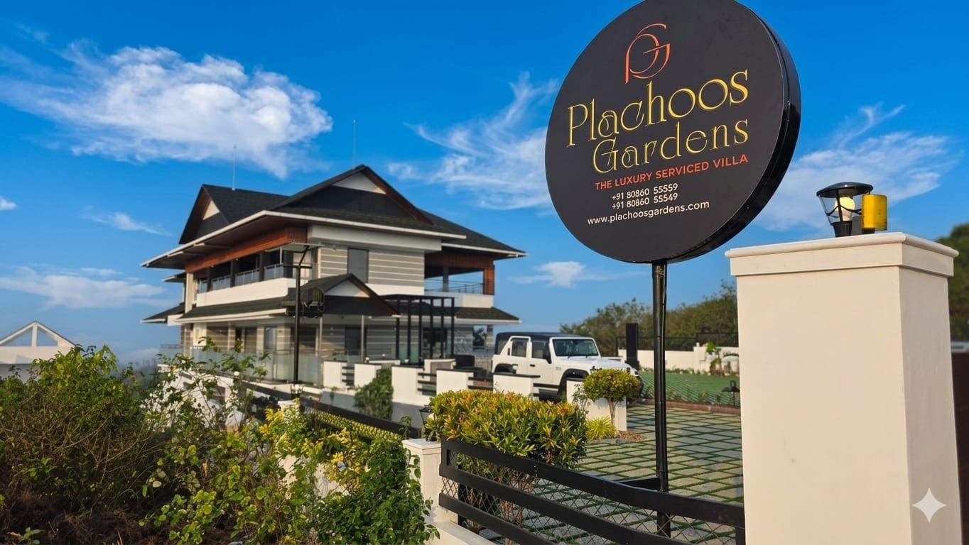 A sign for Plachoos Gardens, a luxury serviced villa with a modern architectural style, a gated entrance, and a clear sky in the background.