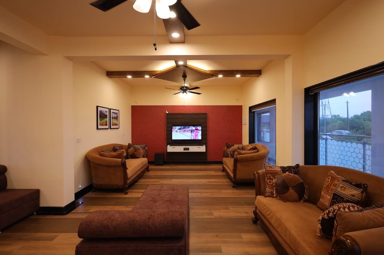 A living room with a flat-screen TV, two sofas, a ceiling fan, and a large window.