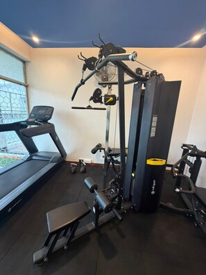 Une salle de sport équipée d’un tapis de course, d’un banc de musculation et de divers appareils d’exercice.