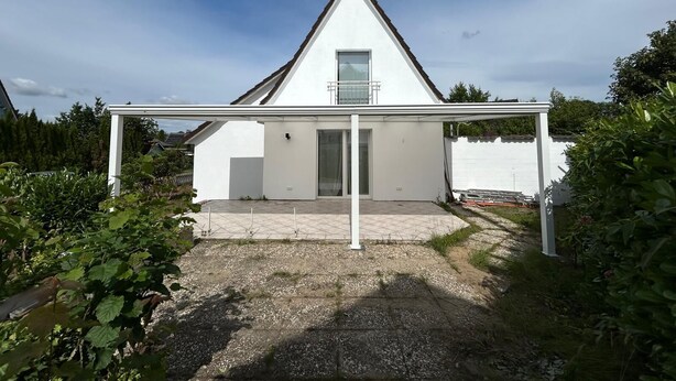 Une maison moderne avec une façade blanche, un toit en pente et un patio couvert.