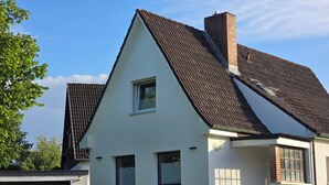 Une maison à deux étages, dotée d’un toit à forte pente, d’un petit porche à l’avant et d’un garage.