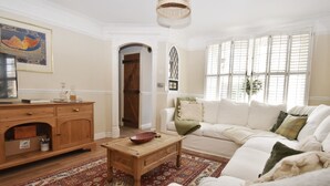 Un salon comprenant un meuble en bois, une table basse, un tapis à motifs et un canapé blanc agrémenté de plusieurs coussins.