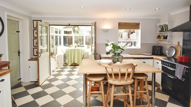 Une cuisine avec un carrelage à motifs, des tabourets de bar en bois, un îlot central et une vue sur le jardin à travers une porte ouverte.