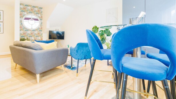 Ein modernes Wohnzimmer mit einem grauen Sofa, blauen Sesseln und einem Flachbildfernseher.