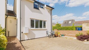 Ein eingeschossiges Haus mit weißer Fassade, einer kleinen Terrasse mit Tisch und Stühlen sowie einem Pflasterweg zum Eingang.
