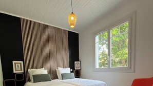Une chambre avec un grand lit, une fenêtre, un fauteuil rouge et un mur recouvert de lambris en bois verticaux.