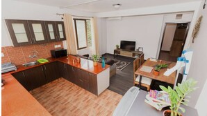 A compact kitchen with a microwave, sink, and cabinets. There is a dining area with a table and chairs, and a television in the background.