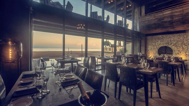 A restaurant with a view of the beach, featuring large windows, wooden tables, and modern decor. - Pledge Scape Negombo (Negombo)