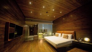 A modern bedroom with a wooden ceiling, a large bed, a TV mounted on the wall, and a bathroom visible through an open door. - Pledge Scape Negombo (Negombo)