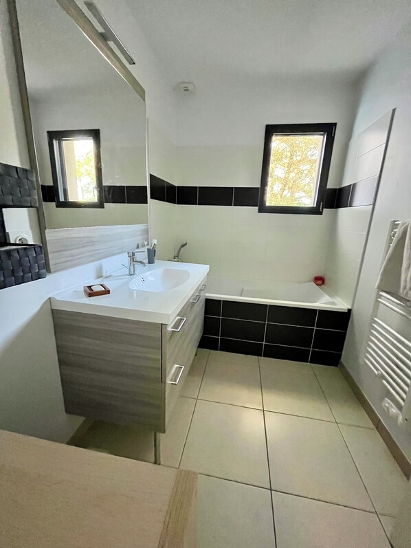 A modern bathroom with a white sink, black and white tiled walls, a bathtub, and a window.