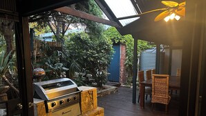 Een terras buiten met een barbecue, rieten meubels en een blauwe deur op de achtergrond.