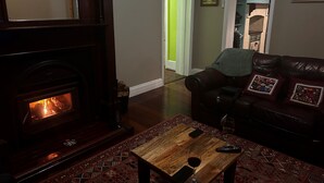 Een gezellige woonkamer met een open haard, een leren bank en een salontafel met een glas wijn en afstandsbedieningen.