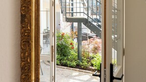 Una habitación con un espejo grande y ornamentado que refleja una escalera, un jardín y la fachada de un edificio.