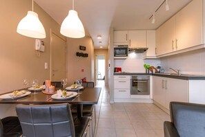A modern kitchen with white cabinets, a microwave, and a stove. There is a dining area with a table set for two, two pendant lights, and a phone on the wall.
