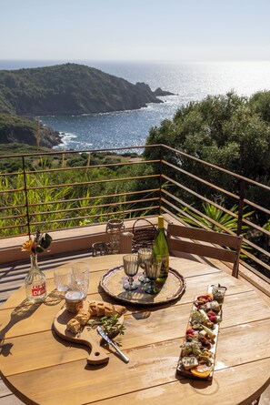A wooden table set with food and drinks on a balcony overlooking a coastal landscape.
