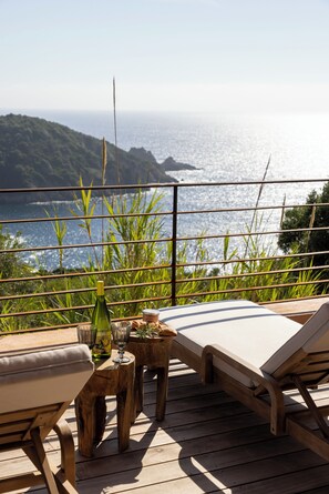 A wooden deck with two lounge chairs and a small table, overlooking a coastal view with greenery and the sea. - House between sea and scrubland near Arone beach in Piana, Corsica (Piana)
