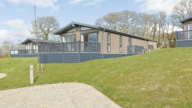 A modern two-story house with a fenced yard, a paved driveway, and a grassy hill.
