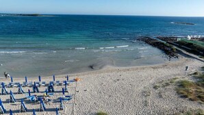 Una playa con filas de sillas azules y sombrillas, un litoral rocoso y una vista despejada del océano.