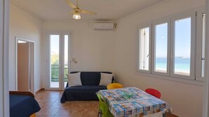 Una habitación con una cama, una mesa con mantel, un ventilador de techo y vistas al mar a través de amplias ventanas.