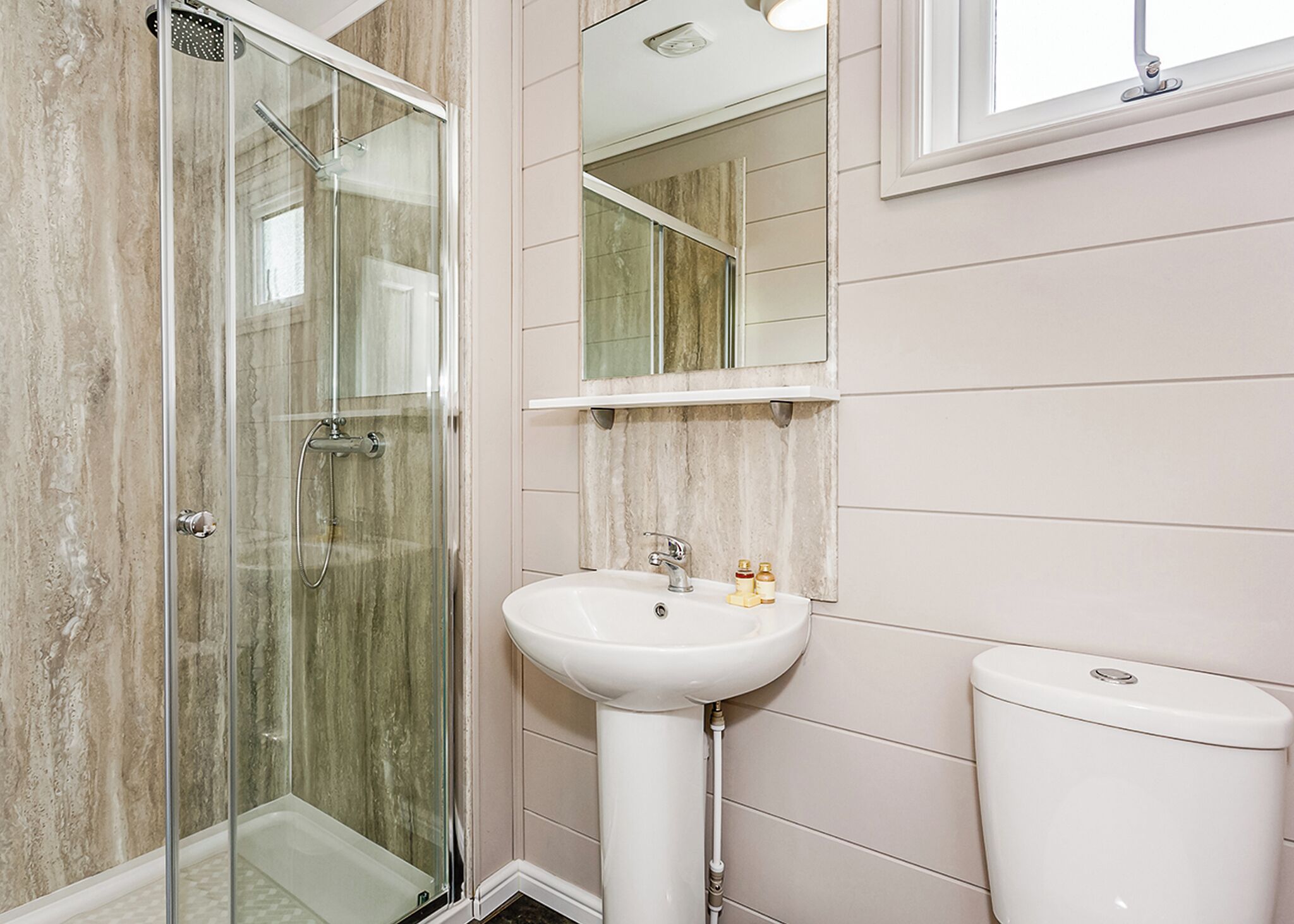 Une salle de bain avec une douche à parois de verre, un lavabo sur colonne et des toilettes.