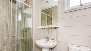 Une salle de bain avec une douche à parois de verre, un lavabo sur colonne et des toilettes.