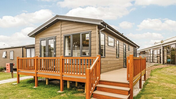 Une maison mobile de plain-pied, dotée d’une terrasse en bois et d’un escalier menant à l’entrée.
