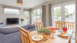 Un coin repas avec une table en bois, des chaises, un téléviseur et de grandes fenêtres ornées de rideaux à motifs.