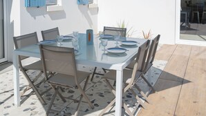 A patio with a glass table and chairs, a green umbrella, and a white wall with blue shutters. - Villa Celestine - Ile d'Oléron - 6 pers - swimming pool (Saint-Denis-d'Oléron)