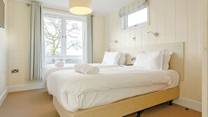 A bedroom with a large bed, a window with curtains, a ceiling light, and a wall-mounted light fixture. - 1 bedroom accommodation in Axminster (Axminster)