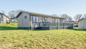 A single-story mobile home with a front deck, a small porch, and a grassy hill in the foreground. - 1 bedroom accommodation in Axminster (Axminster)