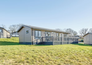 A single-story mobile home with a front deck, a small porch, and a grassy hill in the foreground. - 2 bedroom accommodation in Axminster (Axminster)