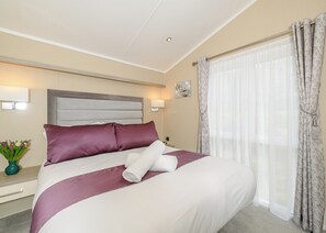 A neatly made bed with a headboard, a bedside table with a lamp, and a window with curtains.