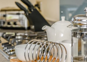 A kitchen area with a white teapot, a white bowl, and a metal strainer on a wooden surface.