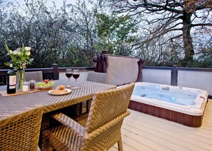 An outdoor patio with a table set for two, a hot tub, wicker chairs, and a view of trees. - Stunning luxury lodge. (Axminster)
