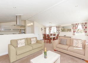 A modern living room with two sofas, a dining table, and a kitchen in the background.