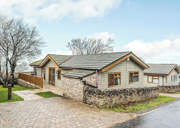 Ein zweigeschossiges Haus mit Stein Fundament, einer Holzterrasse und einem gepflasterten Auffahrt.