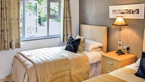 A bedroom with two beds, a nightstand, a lamp, and a window with curtains. - 3 bedroom accommodation in Greystoke, Nr Ullswater (Greystoke, Nr Ullswater)