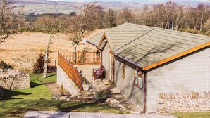 A single-story house with a sloped roof, a wooden deck, and a stone wall. - 3 bedroom accommodation in Greystoke, Nr Ullswater (Greystoke, Nr Ullswater)