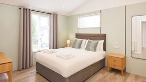 Una habitación de hotel moderna con una cama grande, mesitas de noche, un escritorio y un espejo.