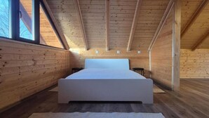 Une chambre avec un grand lit, des murs en bois et un plafond en pente.