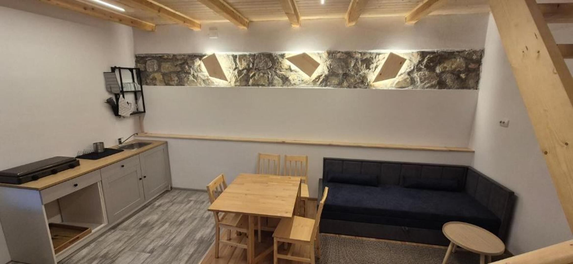 A compact kitchen with a stone backsplash, a dining table with chairs, a dark sofa, and a small round table.