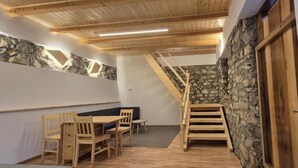 Une pièce avec une table et des chaises de salle à manger en bois, un mur d’accent en pierre, un escalier en bois et une porte dotée d’un interrupteur.