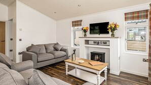 Un salon avec un canapé gris, une table basse en bois, une cheminée et un téléviseur fixé au-dessus.